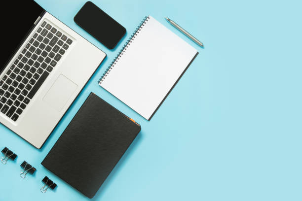 istock Workplace with open laptop, white and black accessory on blue table. Top view and copy space. 1031960236