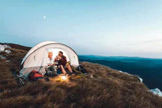 Photo of Senior couple camping in the mountains and eating a snack