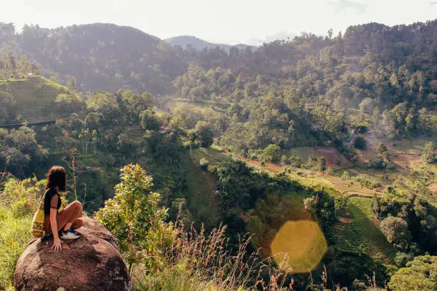 A young woman crouches on a rock as she admires the view of Ella, Badulla District, Sri Lanka.