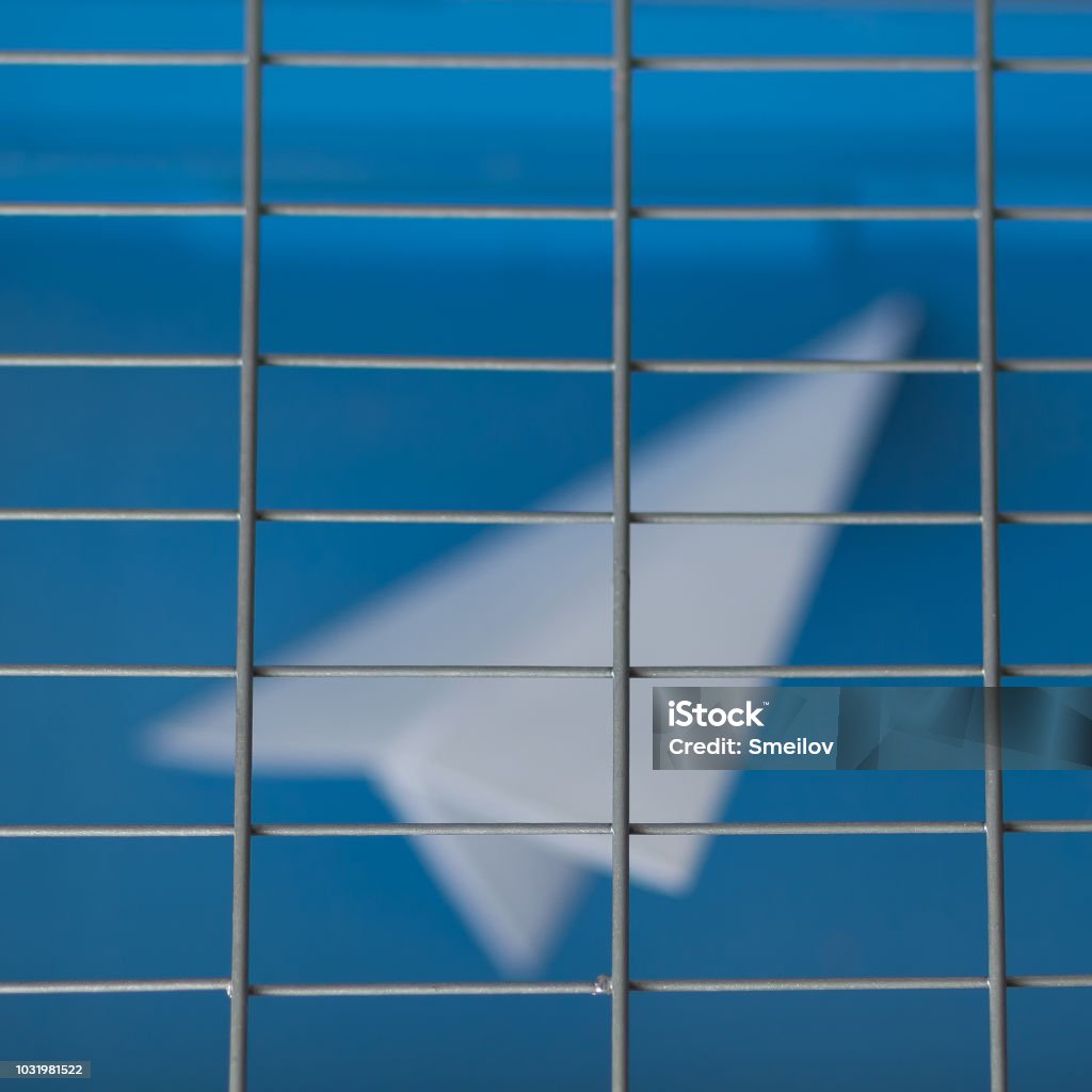 Russia is blocking Telegram: silhouette of a paper plane behind bars on a blue background April Stock Photo