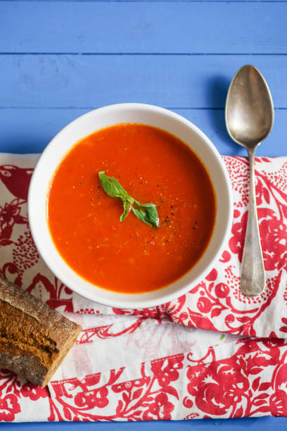 istock Tomato soup garnished with basil leaves served with rye bread on blue wooden table 1031998934