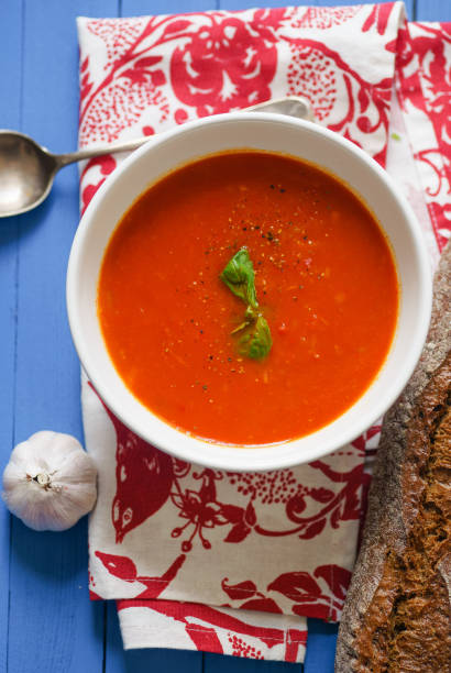 istock Tomato soup garnished with basil leaves served with rye bread on blue wooden table 1031998980