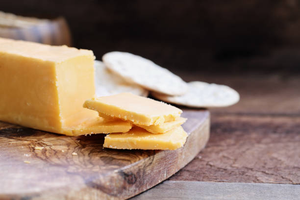 Block of Cheddar Cheese with Slices Block of cheddar cheese and slices over a rustic background.. Extreme shallow depth of field with selective focus on cheese. Water crackers in the background. American Cheese stock pictures, royalty-free photos & images