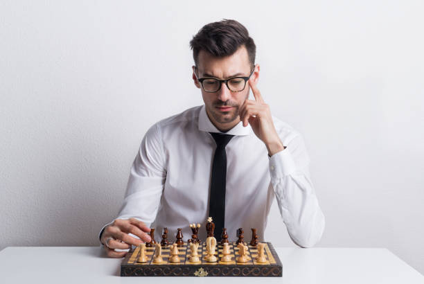 Portrait of a young man in a studio, sitting at the table with chess board game. Portrait of a thoughtful young man with white shirt and necktie in a studio, sitting at the table with a chess board game. challenges face by executors stock pictures, royalty-free photos & images