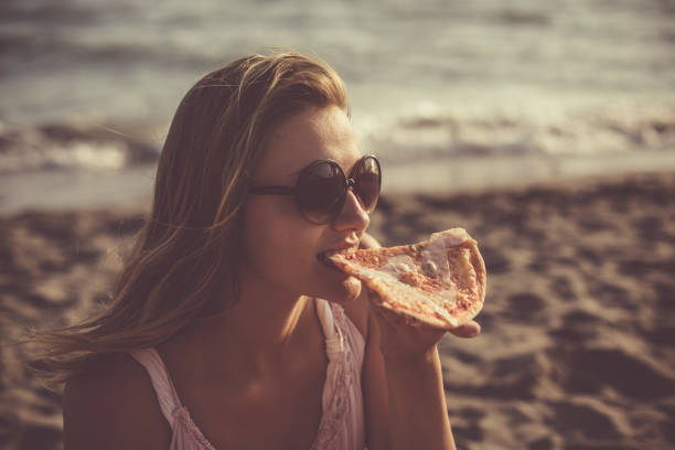 istock Woman eating pizza at the beach 1032007402