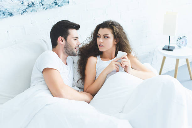 istock high angle view of smiling young man looking at girlfriend using smartphone in bed 1032011804