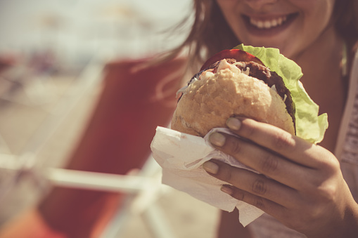 Close-up shot of a happy woman holding a delicious burger outdoors.