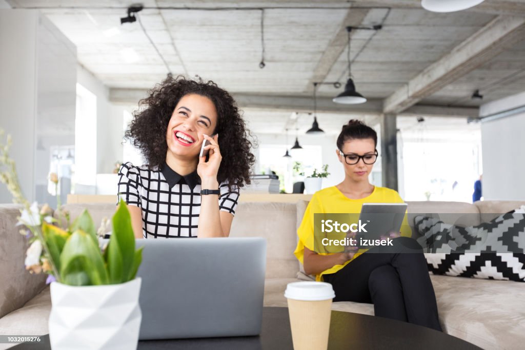 Women working on design office Happy young woman talking on mobile phone with colleagues sitting at side using digital tablet. 20-24 Years Stock Photo