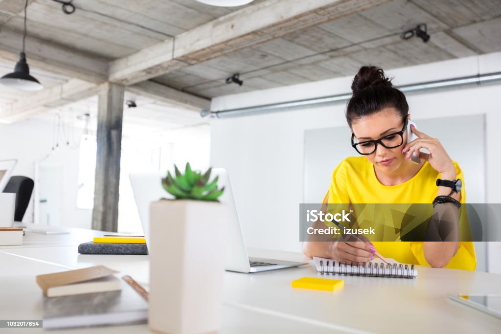 Creative designer working at her desk Designer drawing sketch and talking on cell phone. Female creative professional making a phone call to the client while preparing new design. Customer Stock Photo