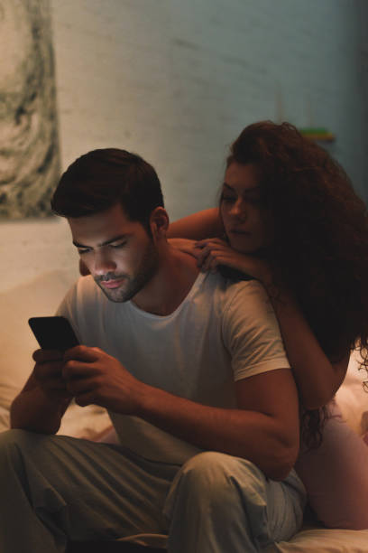 istock young woman looking at boyfriend using smartphone on bed at night 1032023658