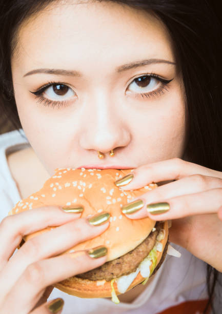 Black long-haired young Asian woman is badly behaving and eats a hamburger.