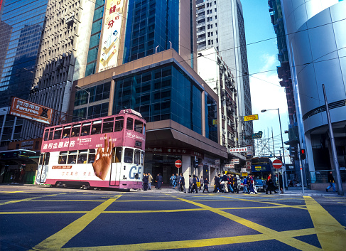 An colourful iconic double decker electric tram crowded with passengers zooming down the road in the busy downtown Central District of Hong Kong Island, China.