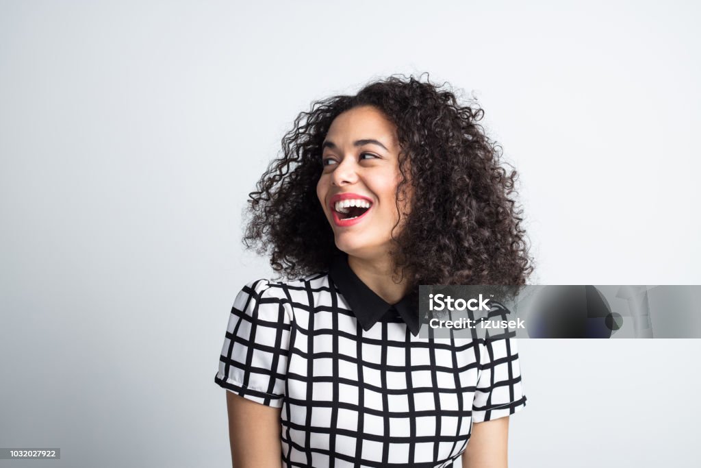 Cute woman looking away and laughing Close up portrait of cute young woman with curly hair looking away and laughing. Cheerful female model looking at copy space on gray background. Women Stock Photo