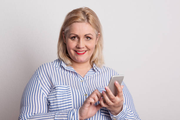 Portrait of an attractive overweight woman with smartphone in a studio. Portrait of an attractive blond overweight woman with smartphone in studio on a white background. big fat lips stock pictures, royalty-free photos & images