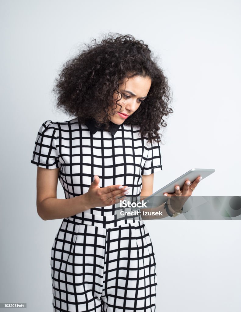 Woman looking seriously at digital tablet Young woman in casual outfit looking at digital tablet seriously against gray background 20-24 Years Stock Photo