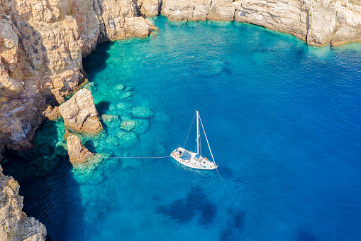 Aerial view of a sailing boat moored in a secluded by with pristine, turquoise waters in the Aegean Sea, Greece