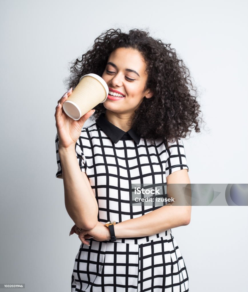 Happy woman drinking coffee Portrait of beautiful young woman drinking coffee from disposable cup against gray background Cheerful Stock Photo