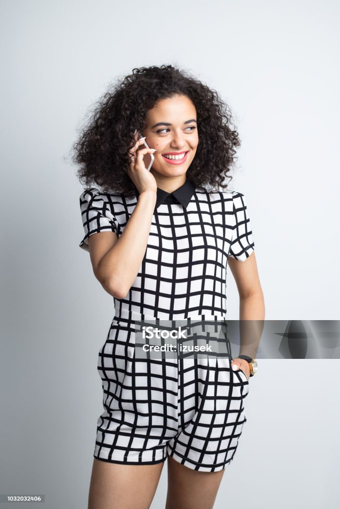 Stylish woman talking over phone Stylish young woman in standing against gray background and talking over mobile phone 20-24 Years Stock Photo