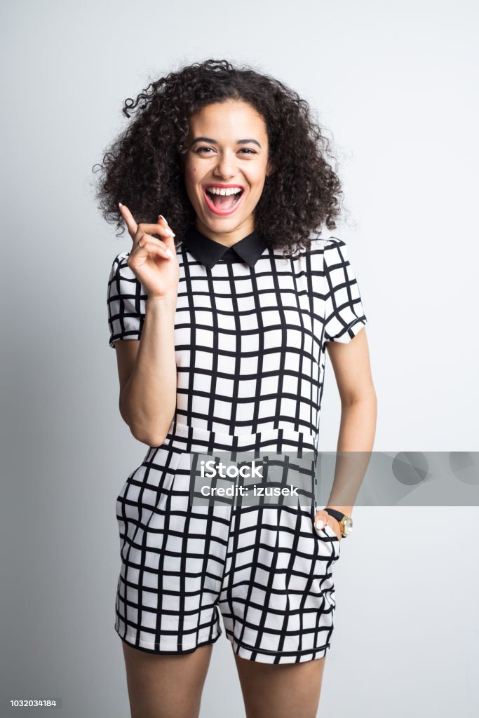 Surprised woman showing copy space Vertical portrait of cheerful young woman in casual wear pointing away on gray background. Surprised female in stylish outfit pointing away. 20-24 Years Stock Photo