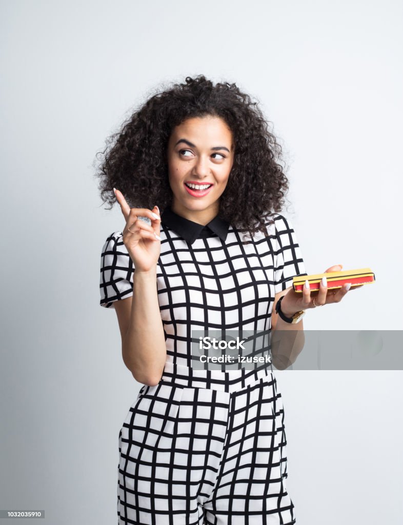 Woman holding a book and pointing away Portrait of attractive young woman holding a book and pointing away on grey wood background Asking Stock Photo