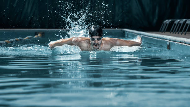 dynamic and fit swimmer in cap breathing performing the butterfly stroke - blue water swimming pool sports and fitness imagens e fotografias de stock