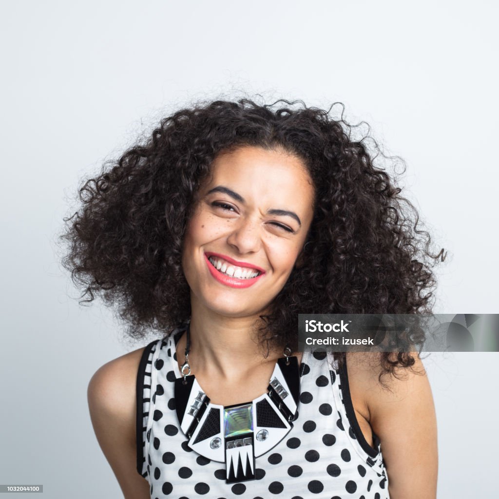 Cute woman winking with beautiful smile Close up portrait of attractive young woman with curly hair winking on white background 20-24 Years Stock Photo