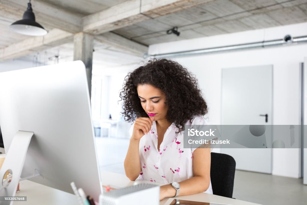 Female programmer working at her desk in office Female programmer working at her desk in office. Mixed race woman thinking while working at modern office. Adult Stock Photo