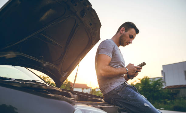 Man next to a broken down car Young man is text messaging, standing next to a broken down car waiting telephone on the phone frustration stock pictures, royalty-free photos & images