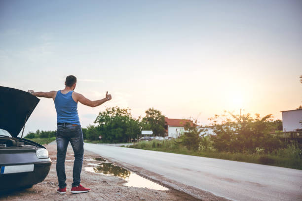 istock Man hitchhiking next to a broken car 1032062562