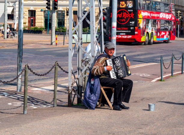 A street musician playing a piano accordion near the harbour in Helsinki, Finland’s capital city, on a sunny summer day. In the background is a double-decker Hop-On-Hop-Off bus, taking tourists on a tour of the city.