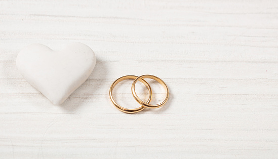 Love and marriage concept.  Close up view of golden wedding rings and a white heart, copy space, isolated, on a white wooden background.