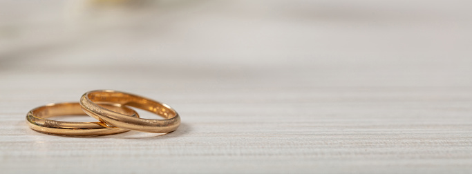 A pair of golden wedding rings on white wooden background, banner, copy space
