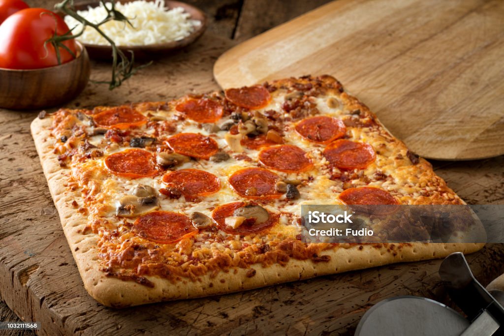 Square Crust Flatbread Pizza A delicious square crust flatbread pizza with pepperoni, bacon and mushrooms on a rustic wood table top. Pizza Stock Photo