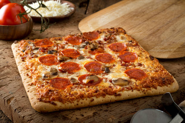 Square Crust Flatbread Pizza A delicious square crust flatbread pizza with pepperoni, bacon and mushrooms on a rustic wood table top. flatbread photos stock pictures, royalty-free photos & images