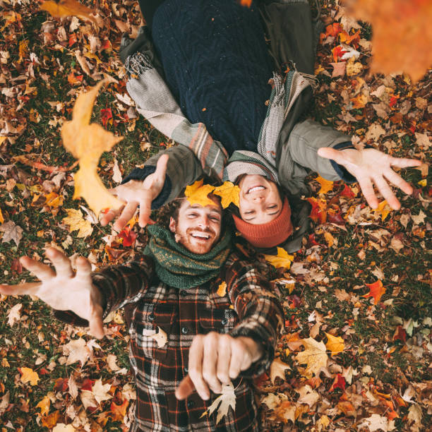 Young Canadian Heterosexual Couple Enjoying A Beautiful Autumn Day Outdoors Cute young couple playing with autumn leaves. canadian culture photos stock pictures, royalty-free photos & images