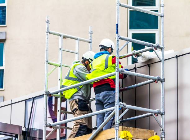 two builders in retro-reflective clothing and helmets on scaffolding are engaged in repair work - uk scaffolding construction building activity imagens e fotografias de stock