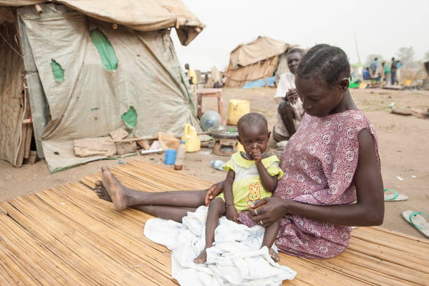 вместе со своей дочерью женщина сидит в лагере для перемещенных лиц в джубе, южный судан. - slum living фотографии стоковые фото и изображения