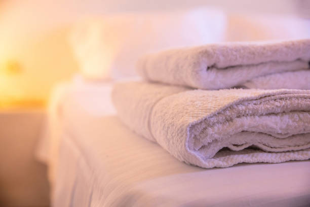 istock Close-up of white towels on a bed on a blurry with warm light  background. 1032150724
