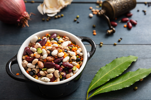 Flat lay of assortment of legumes on black wooden tabletop background, in enamel bowl