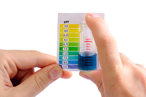 Man determining water pH by comparing the color of liquid in testing vials with attached color scale. Water is alkaline