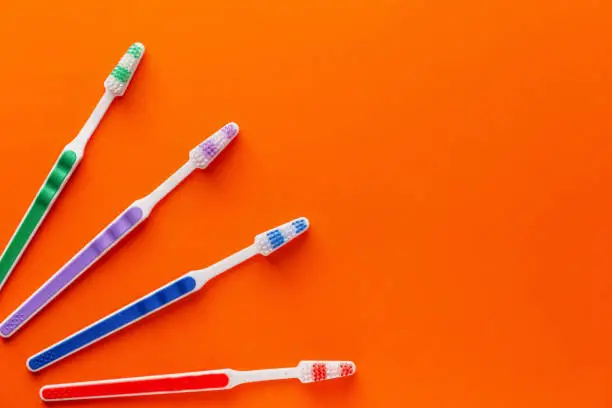 Four color toothbrushes an orange background, top view, copy space