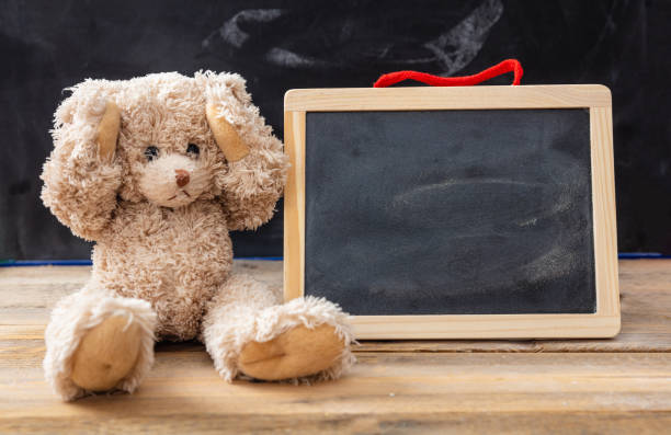 Bullying at school or learning difficulties concept. Teddy bear covering ears and a blank blackboard, space for text