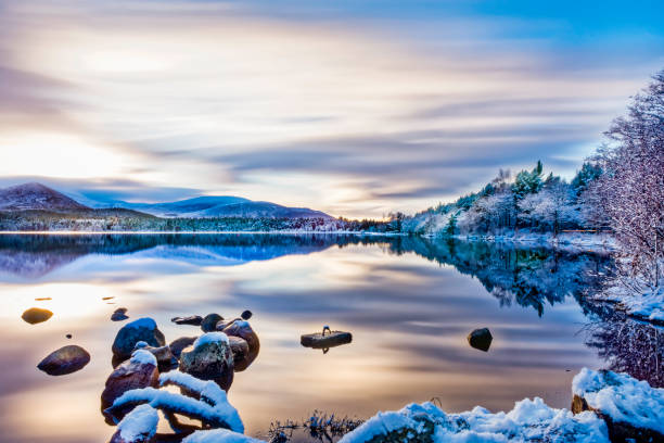 dia lindo invernos com suaves nuvens, neve em árvores e rochas, reflexões sobre águas calmas no loch morlich, aviemore - winter lake snow water - fotografias e filmes do acervo