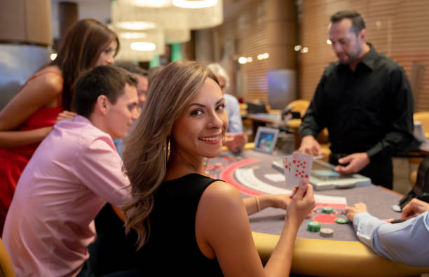 retrato de hermosa mujer sosteniendo las cartas ganadoras en la mesa de blackjack mientras mira a la cámara sonriendo - currency women luxury wealth fotografías e imágenes de stock