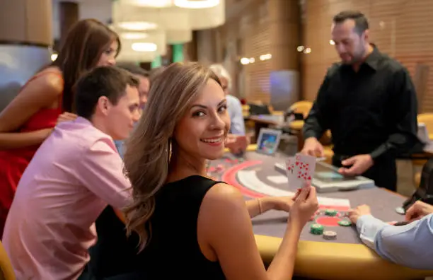 Photo of Portrait of beautiful woman holding the winning cards at the blackjack table while looking at camera smiling