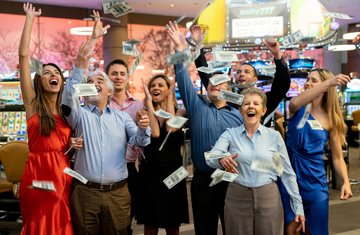 Excited group of adults and seniors celebrating a big win at the casino throwing money to the air all looking very happy