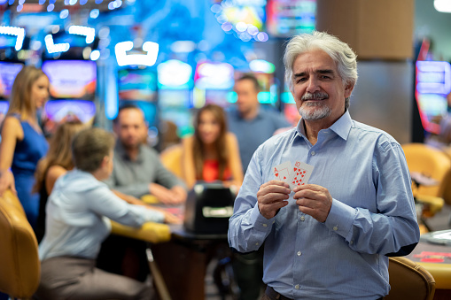 Senior man at the casino holding a ten and an ace while looking at camera smiling - Focus on foreground