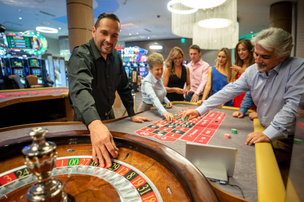 casino worker ready to release the ball on the roulette wheel while others are still placing bets on table - casino worker imagens e fotografias de stock
