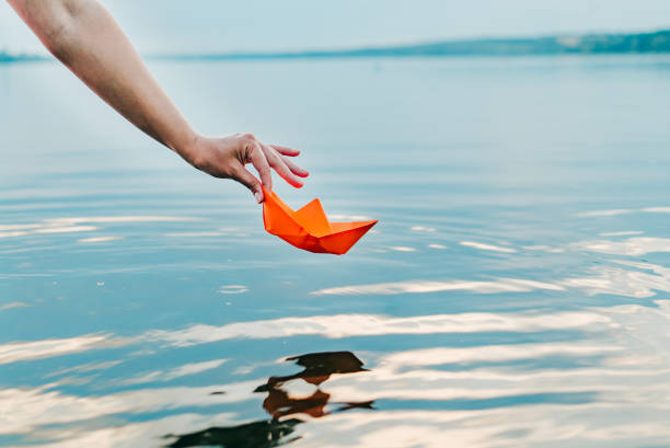 la chica deja a su barco de papel al agua con su mano. - sea water single object sailboat fotografías e imágenes de stock