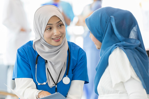 Caring female doctor wearing a hijab talks with an expectant mother during a prenatal exam.